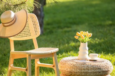 Dergi, kahve fincanı ve vazo dolusu rahat sandalye parktaki hasır masada, açık havada.