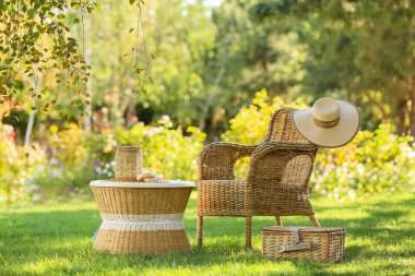 Sepetli rahat bir hasır koltuk, şık bir şapka ve dekorasyon parktaki kahve masasında, açık havada.
