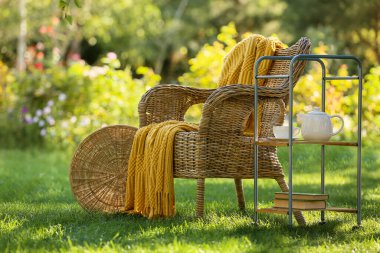 Kitaplar ve çaydanlıkla dolu rahat hasır koltuk parkta, açık havada servis arabasının üzerinde.