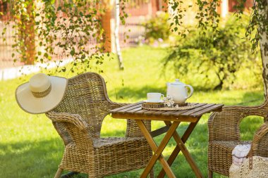 Rahat hasır koltuklar şık şapkalar, papatya çiçekleri ve çaydanlık parkta, açık havada kahve masasında.
