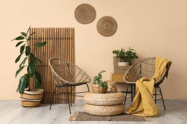 Koltukları, katlanan ekranı, çiçekleri, komodini ve bej duvarın yanındaki hasır masasını olan bir oda.