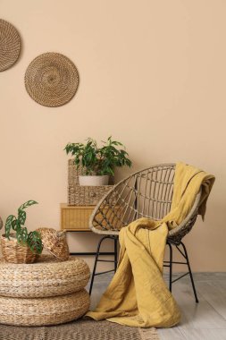 Koltuklu, çiçekli, komodinli ve bej duvarın yanındaki hasır masalı bir oda.