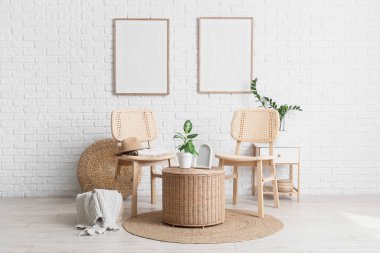 Oturma odasının içinde sandalyeler, ev bitkileri, şilteler, çerçeveler ve beyaz tuğla duvarın yanındaki hasır masa.