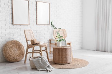 Oturma odasının içinde sandalyeler, ev bitkileri, şilteler, çerçeveler ve beyaz tuğla duvarın yanındaki hasır masa.