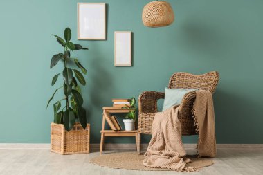 Hasır koltuk, ev bitkileri, asılı çerçeveler ve mavi duvarın yanındaki merdivenle ilgili kitaplarla dolu bir oda.