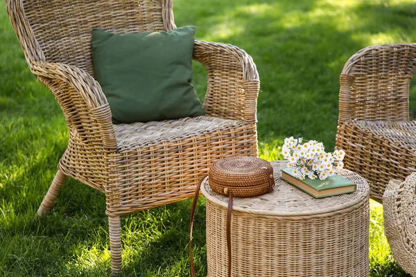 Rahat hasır koltuklar, papatya çiçekleri, kitap ve çanta parkta, açık havada kahve masasında.