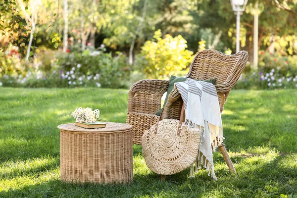 Rahat hasır koltuk, çantalar, papatya çiçekleri ve parktaki sehpanın üzerinde kitap.