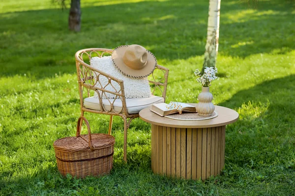 Sepeti, kitabı ve vazosu olan rahat bir hasır koltuk. Parktaki kahve masasında, açık havada.