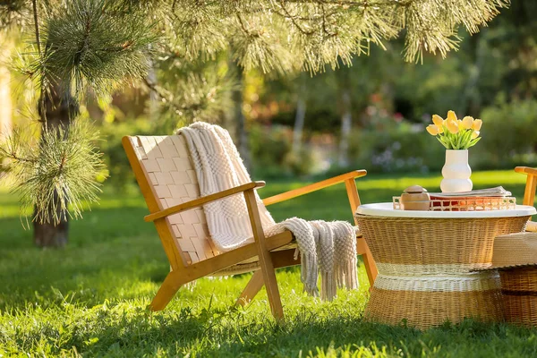 Rahat hasır koltuk, dergiler ve vazo çiçekleri parktaki kahve masasında, açık havada.