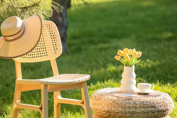 Dergi, kahve fincanı ve vazo dolusu rahat sandalye parktaki hasır masada, açık havada.