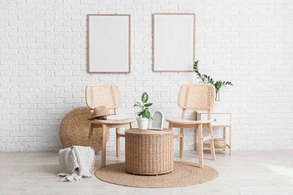 Oturma odasının içinde sandalyeler, ev bitkileri, şilteler, çerçeveler ve beyaz tuğla duvarın yanındaki hasır masa.