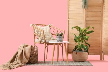 Masası, bitkileri ve pembe arkaplanı olan hasır koltuk.