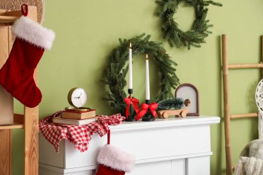 Noel çelenkleriyle mum yakmak ve yeşil duvarın yanındaki şöminede dekorasyon yapmak.