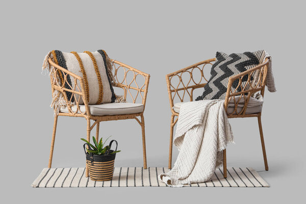 Wicker armchairs with plant and rug on light background