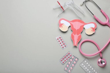 Steteskoplu jinekolojik spekulum, kağıt rahim ve gri arka planda haplar.