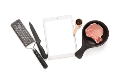 Mutfak aletleri ve beyaz arka planda eti olan dijital tarif kitabı.