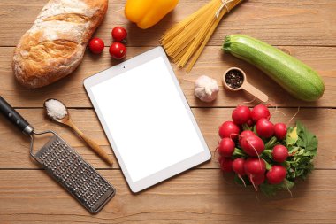 Mutfak gereçleri ve ahşap arka plandaki malzemelerle birlikte dijital tarif kitabı.