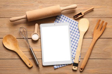 Ahşap arka planda peçete ve mutfak aletleri olan dijital tarif kitabı.