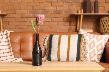 Oturma odasındaki sehpanın üzerinde şişe içinde tropik bir çiçek. Yakın çekim.