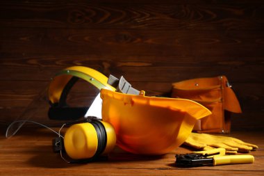 Sert şapka, koruyucu kulaklıklar, kablo sökücü ve tahta arka planda eldivenler, yakın plan.