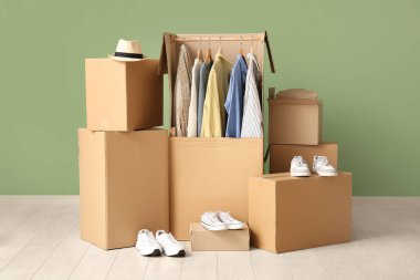 Yeşil duvarın yanında erkek kıyafetleri ve ayakkabıları olan gardırop kutuları.