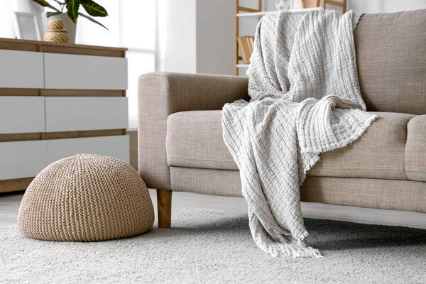 Knitted pouf near grey sofa in living room