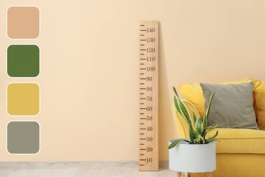 Sarı kanepe, bitki ve stadyum, odadaki bej duvarın yanında. Farklı renk desenleri