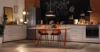 Tezgahları, yemek masası ve geceleri parlayan lambaları olan şık bir mutfak.