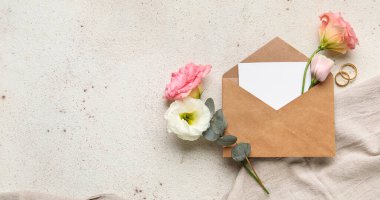 Zarflı kompozisyon, boş kart, alyans ve açık arkaplanda östoma çiçekleri