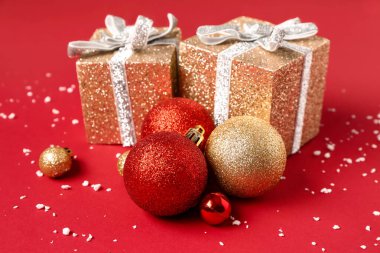 Kırmızı arka planda Noel topları ve hediye kutularıyla kompozisyon, yakın plan.