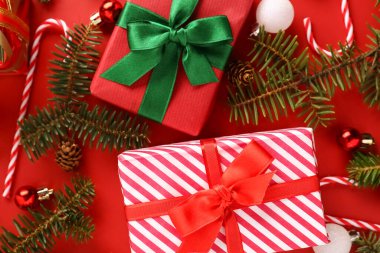 Toplu Noel hediyesi kutuları, köknar ağacı dalları ve kırmızı arka planda şeker kamışı oyuncakları