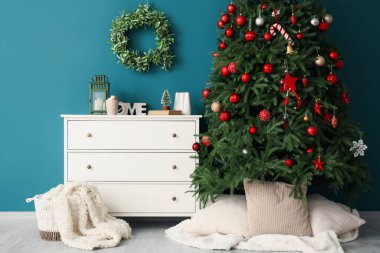 Şifoniyerli Noel ağacı ve mavi duvarın yanındaki süslemeler.