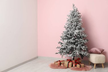 Hediye kutularıyla Noel ağacı ve pembe duvarın yanında yastıklı puf.