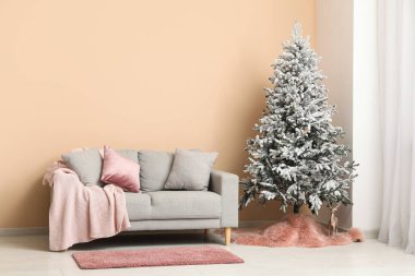 Yastıklı, ekoseli, süslü Noel ağacı ve oturma odasının içinde ren geyiği olan rahat bir kanepe.