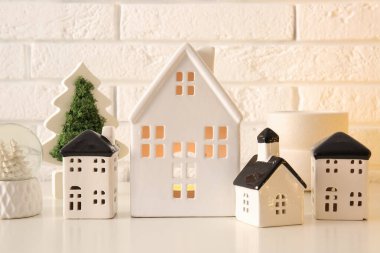 Beyaz tuğla duvarın yanındaki masada Noel dekoru olan ev şekilli mum tutucular, yakın plan.