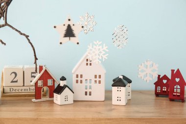 Mavi duvarın yanındaki masada kar taneleri olan ev şeklinde mum tutucular.