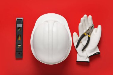 Beyaz başlıklı ruh seviyesi, kırmızı arka planda eldivenler ve pense.