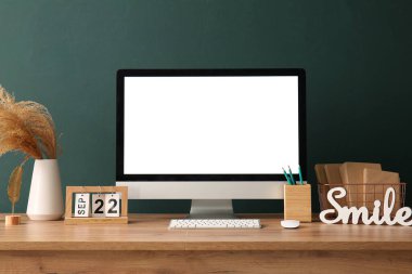 Takvim ve kitaplarla dolu boş bilgisayar monitörü yeşil duvarın yanında.