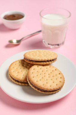 Çikolata kremalı lezzetli sandviç bisküvileri ve pembe arka planda bir bardak süt.