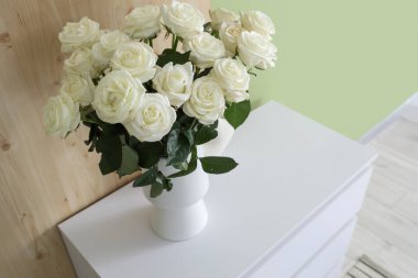 Yeşil duvarın yanındaki çekmecelerde beyaz güller olan vazo, yakın plan.