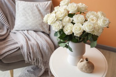 Oturma odasındaki masada beyaz güllü vazo.