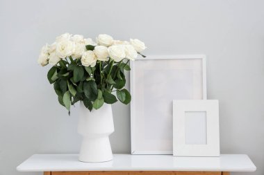 Beyaz güller ve boş çerçevelerle aydınlık duvarın yanındaki masada.