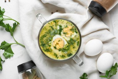 Beyaz arka planda yumurta, baharat, defne yaprağı ve maydanozlu lezzetli yeşil borş çorbası.