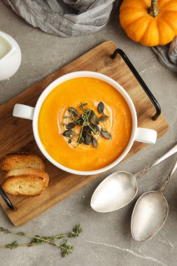 Gri grunge arka planda tohumlu ve otlu lezzetli balkabağı kremalı çorba, yakın plan.