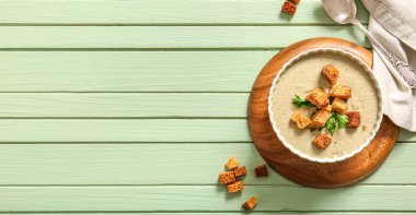 Yeşil ahşap arka planda kıtır kıtır kremalı bir kase çorba.