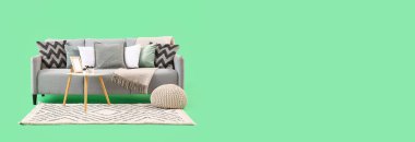 Masalı gri kanepe, yeşil arka planda puf ve halı.