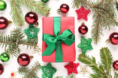 Noel toplarıyla hediye kutusu, köknar ağacı dalları ve beyaz arka planda dekoratif yıldızlar.