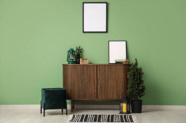 Pouf, köknar ağacı, içinde Noel feneri olan çekmeceler ve yeşil duvarın yanındaki çerçeve.