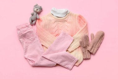 Pembe arka planda şık çocuk süveteri, kot pantolon, eldiven ve oyuncak