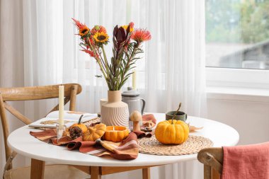 Sonbahar çiçekleri, balkabakları ve yanan mumlarla dolu yemek masası.